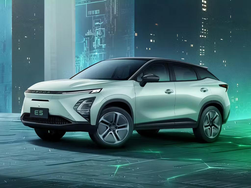 Front three-quarter view of the OMODA E5 electric SUV in white, featuring sharp LED headlights, bold front grille design and sculpted bodywork against a futuristic cityscape backdrop.
