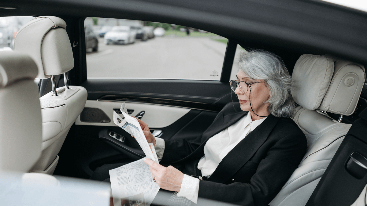 Senior businesswoman sitting in luxury car using a smartphone