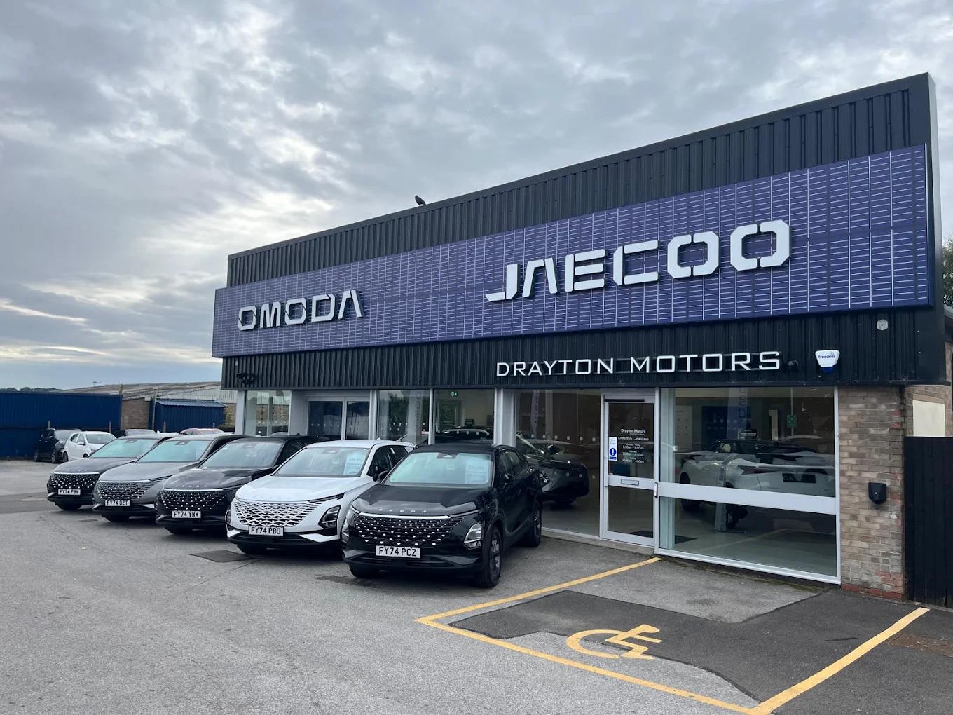 Drayton Motors OMODA and JAECOO Grantham dealership exterior with a row of new SUVs displayed on the forecourt beneath branded signage