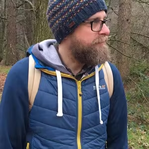Person wearing a beanie hat and backpack standing in a woodland setting.