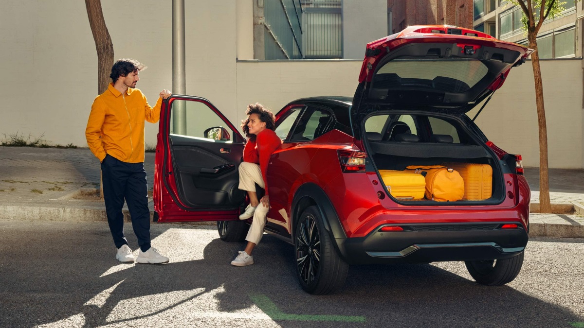 A couple with a red Nissan Juke. The boot is open and is filled with luggage.