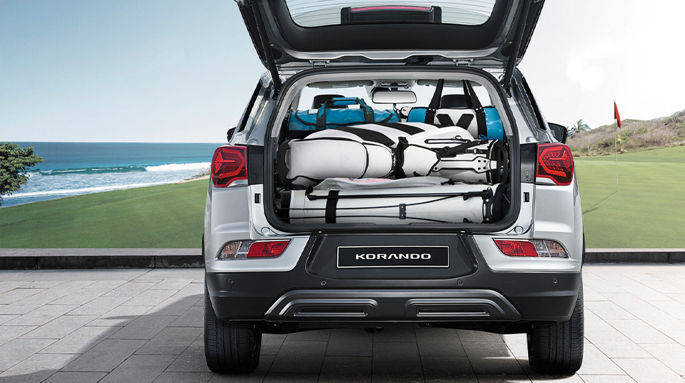 White SsangYong Korando at a coastal golf course with the boot open showing it full of golf equipment