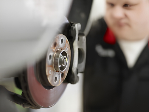 Technician inspecting a vehicle brake disc and caliper during servicing.