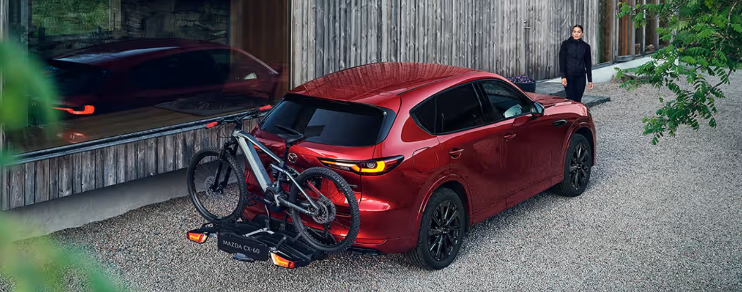 Red Mazda CX-60 with a bike carrier parked outside a modern house.