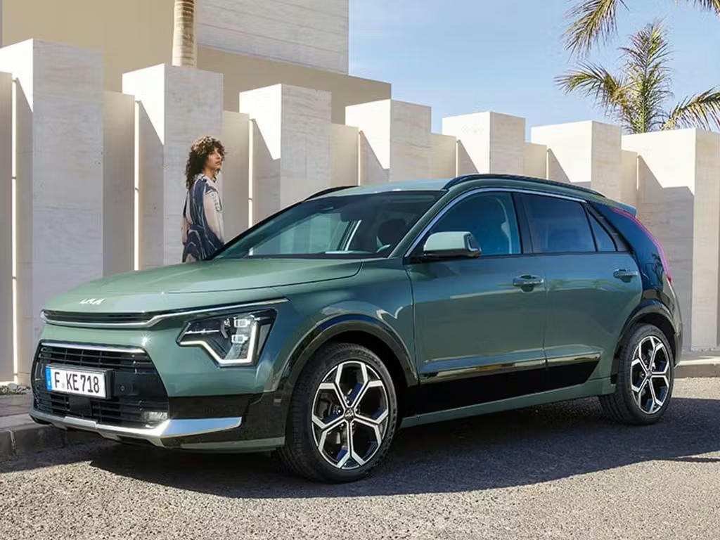 Front three-quarter view of the Kia Niro in sage green, featuring distinctive boomerang-shaped LED headlights, bold two-tone alloy wheels and sculpted crossover bodywork.