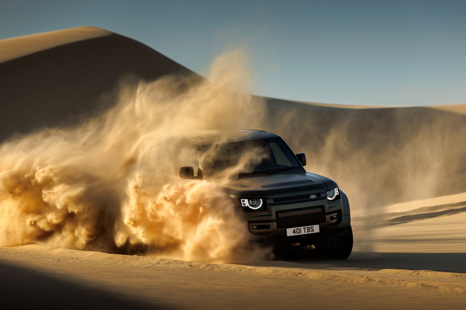 Land Rover Defender powering through sand dunes.