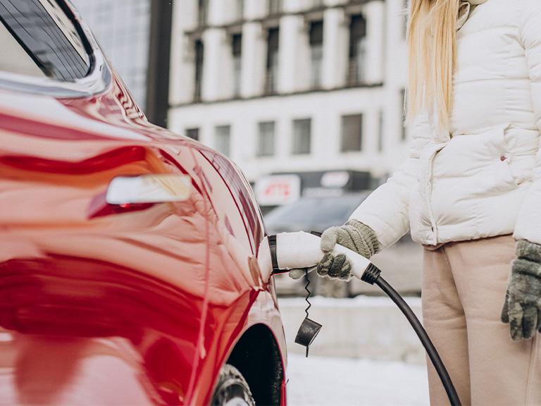 woman charging red electric car in icy weather