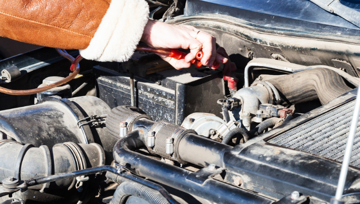 person jump starting a car battery wearing a brown leather jacket