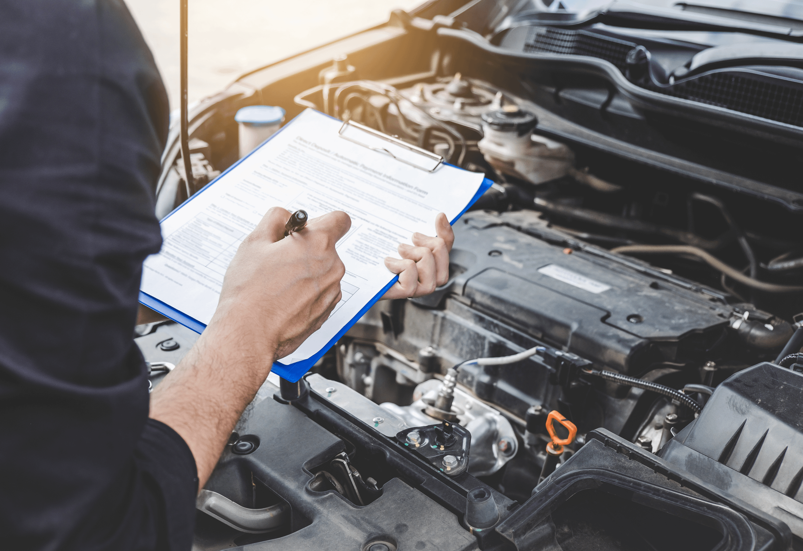 Man stood in front of a car with the bonnet raised, holding a clipboard and pen.