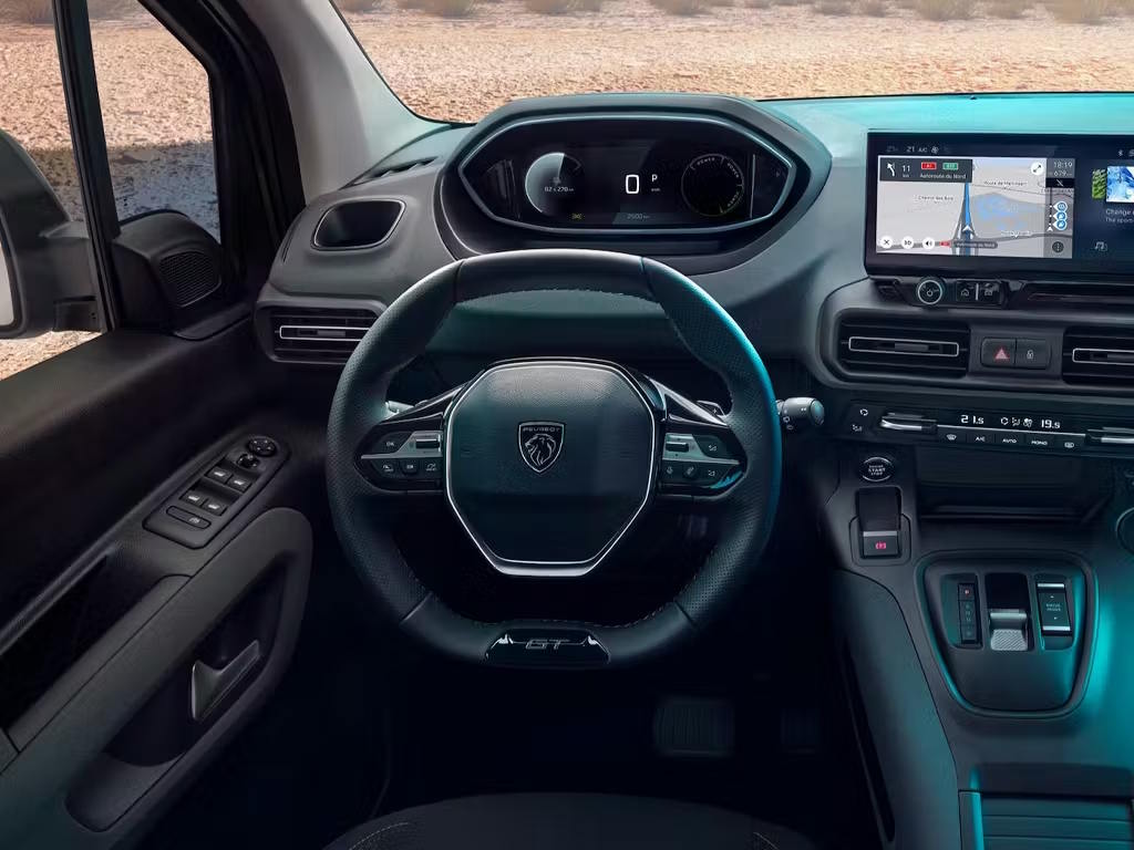 Interior view of the Peugeot E-Rifter electric MPV, featuring the compact steering wheel, digital instrument cluster, central touchscreen with navigation and ambient teal lighting accents.