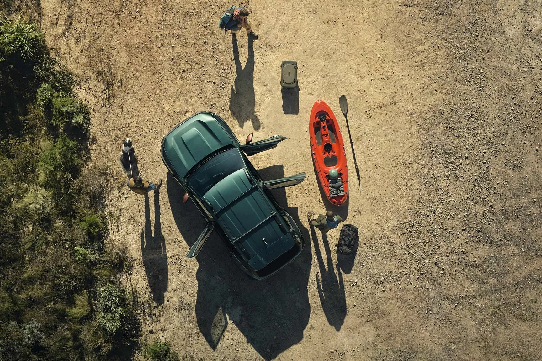 Dacia Duster viewed from above with doors open, parked on dry ground next to a kayak and outdoor gear, with people preparing for an activity.