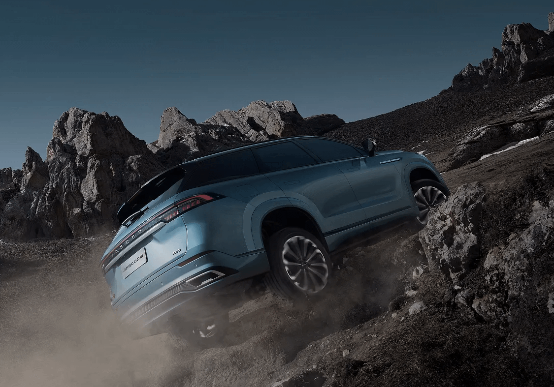 Rear three-quarter view of a Jaecoo J8 navigating rocky terrain with dust trailing behind.