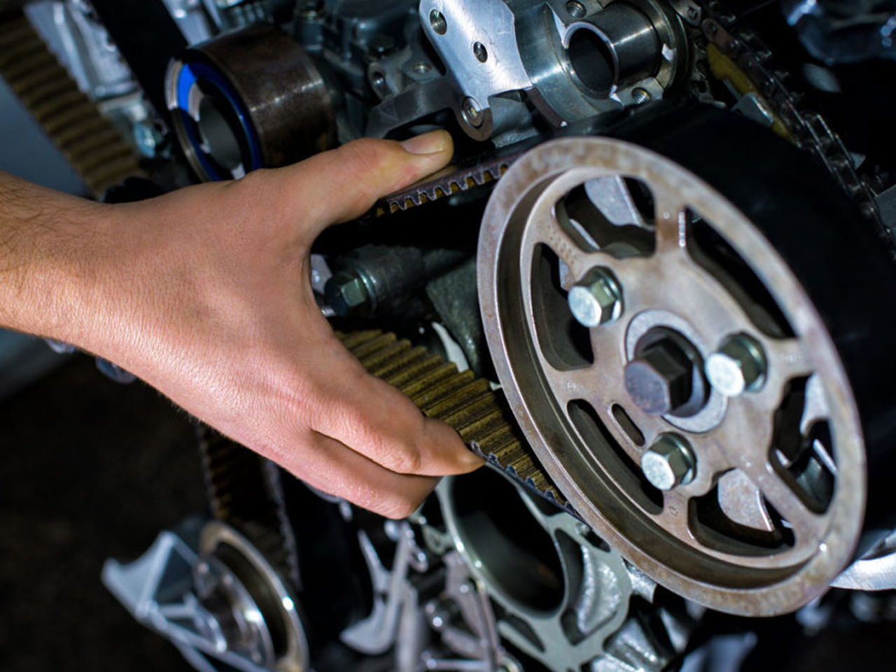 Close-up of a technician's hand fitting a timing belt around the camshaft pulley during engine servicing, showcasing precision mechanical work.