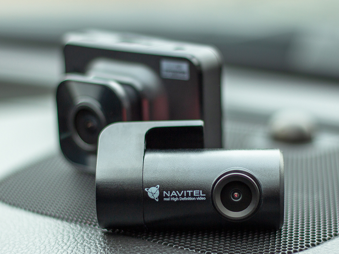 Navitel compact in-car dashcam mounted on a windshield, with a secondary camera unit visible in the background.