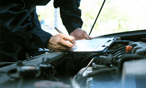 Mechanic leaning on open car bonnet writing on clipboard