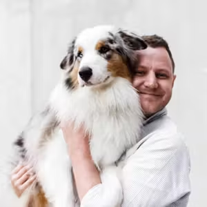 Portrait of a person cuddling a long-haired dog against a neutral background.