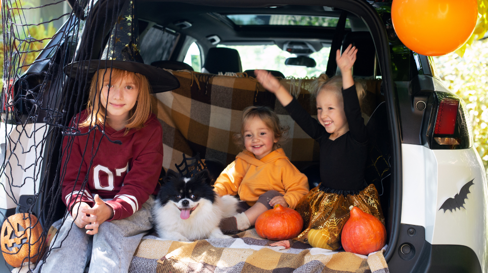 Children and a small dog sitting in the boot space of a car that's been decorated for Halloween