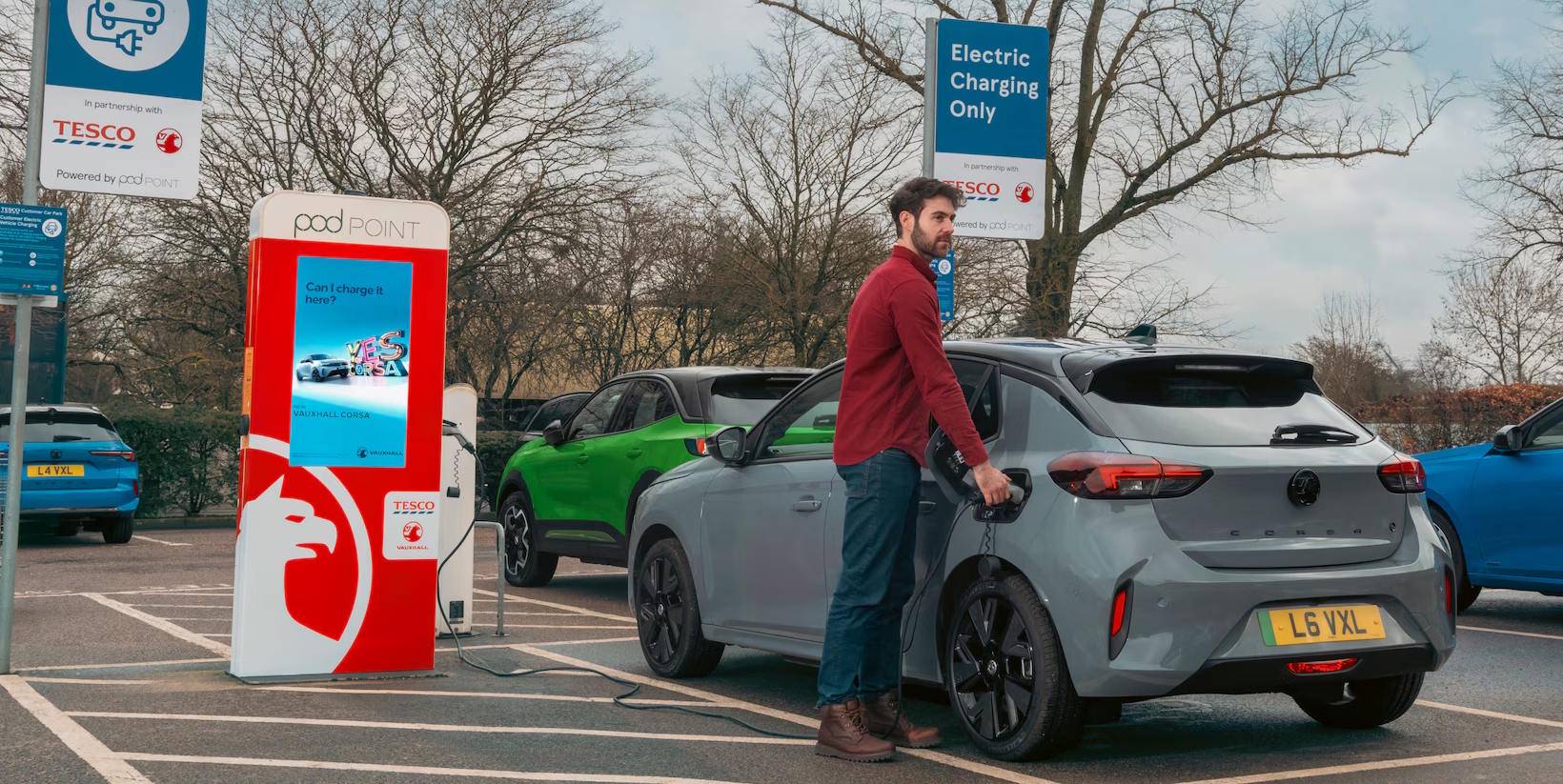 Man charging a grey electric car at a public Pod Point charging station.