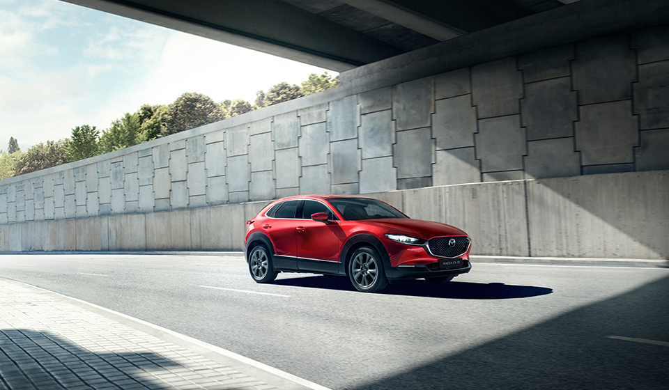 Red mazda cx-30 suv driving fast down a main road.
