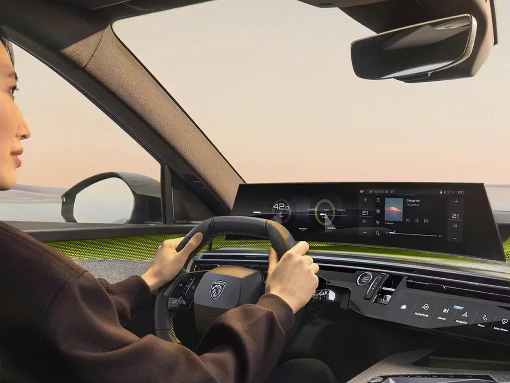 Driver's perspective inside the Peugeot E-5008, showcasing the panoramic i-Cockpit with curved digital display, compact steering wheel and striking lime green ambient lighting accents.