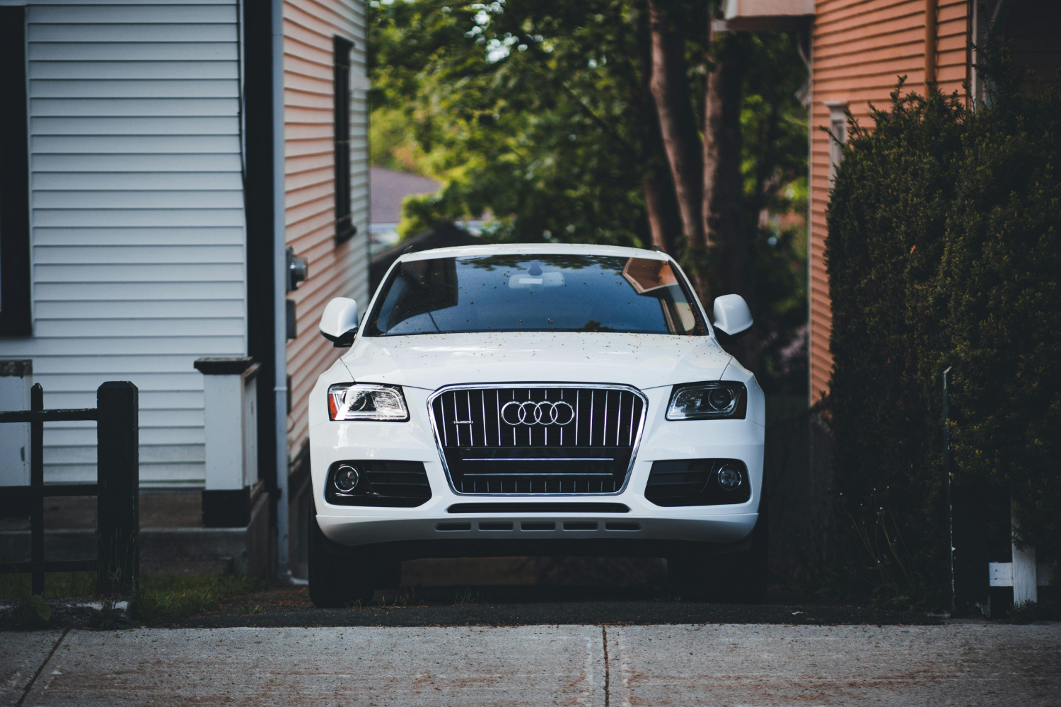 White Audi SUV parked in narrow residential driveway.