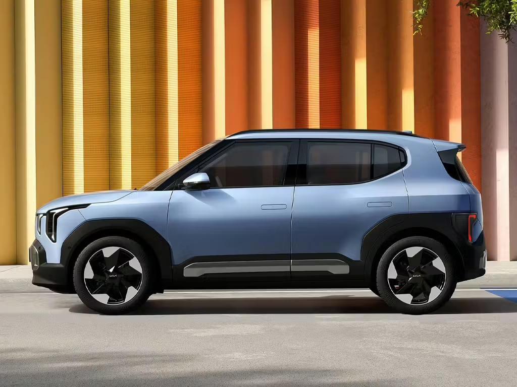 Side profile view of the Kia EV2 compact electric SUV in pale blue, featuring distinctive angular headlights, black body cladding and bold geometric alloy wheels.