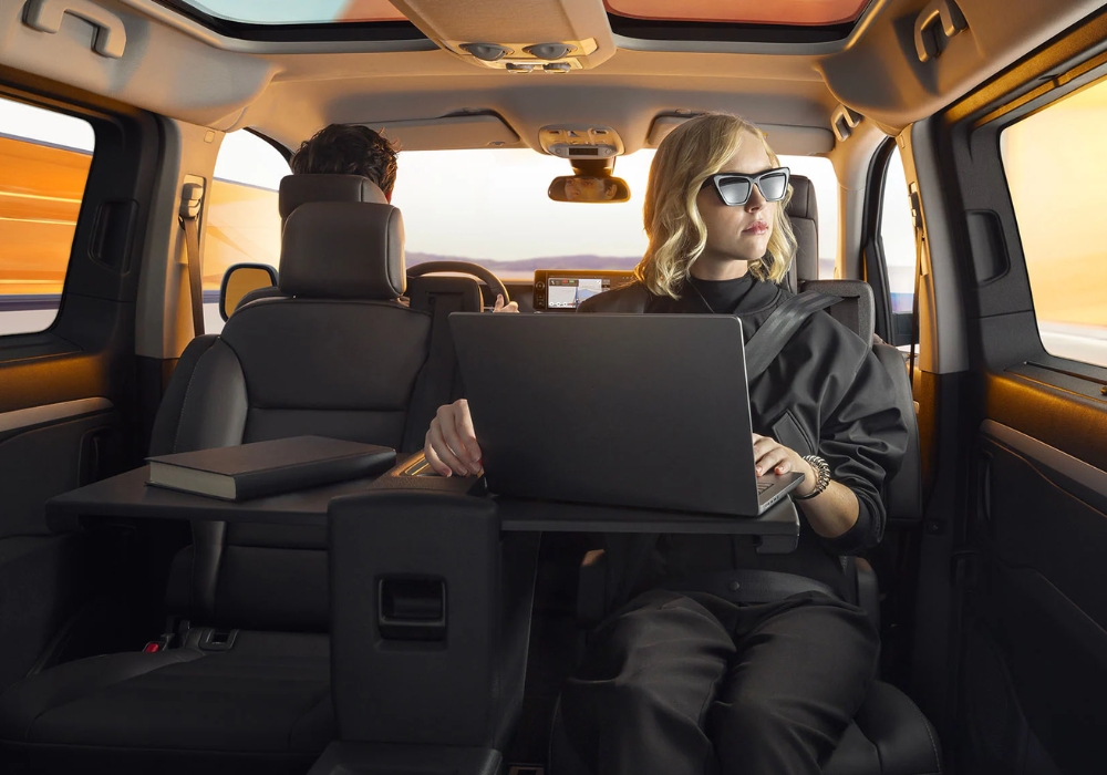 Passenger seated in the rear of Peugeot E-Traveller using a laptop on a fold-out table inside the cabin.