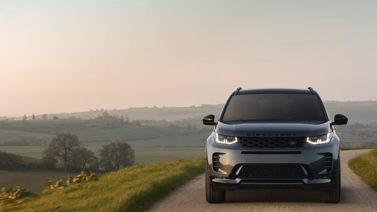 Front view of a Land Rover Discovery Sport driving along a rural road at sunset.