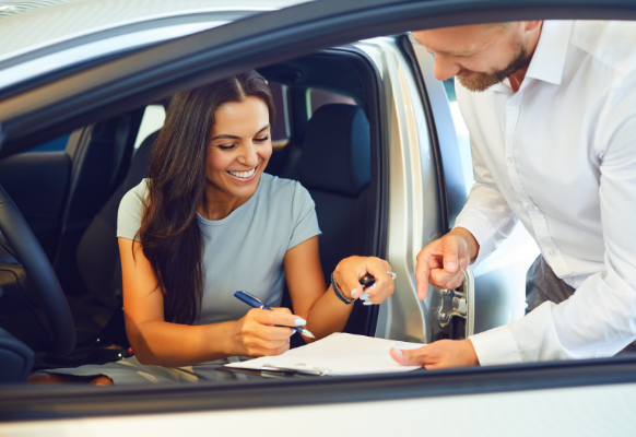 Woman sat in a new car receiving keys and signing documents.