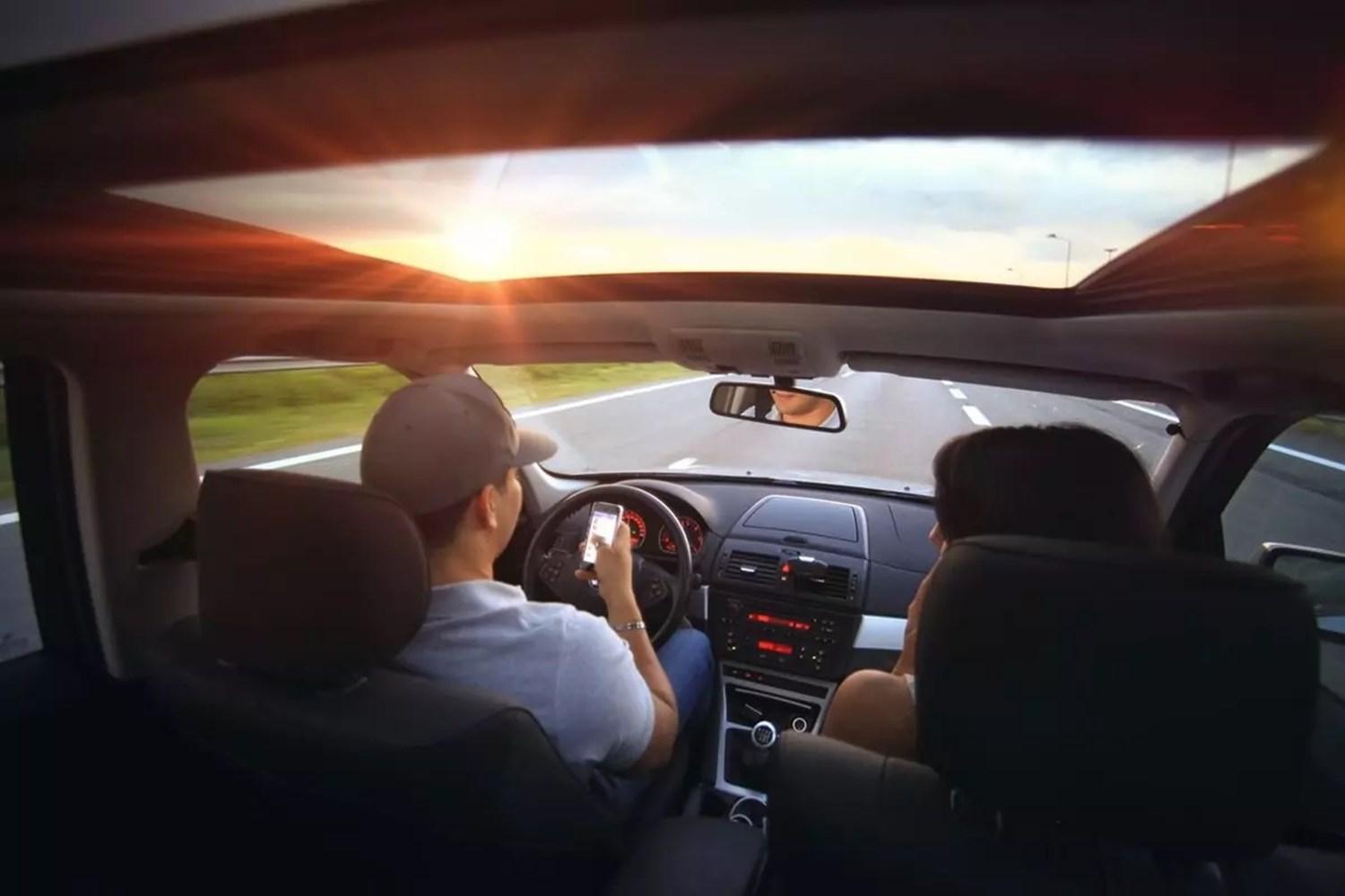 Man driving down road with mobile phone out 