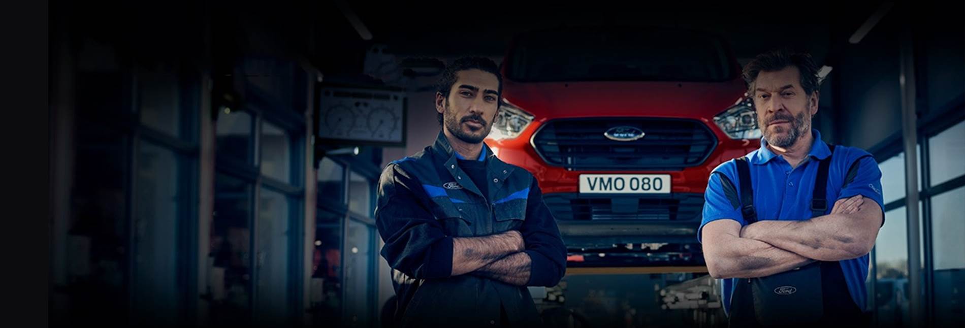 Two Ford mechanics standing in front of an elevated Ford car undergoing a Ford Pro service