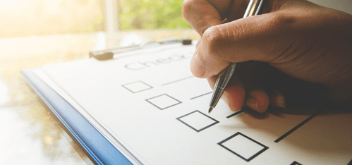A close-up of a checklist with a hand holding a pen
