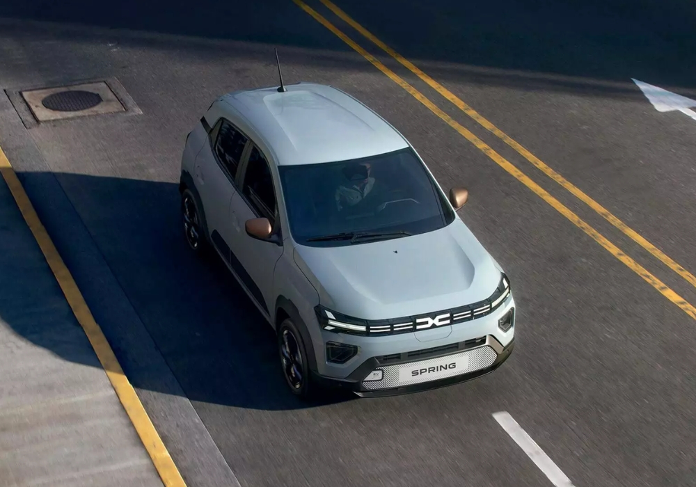 Dacia Spring driving along a city street from an overhead angle, highlighting compact electric design in an urban setting.