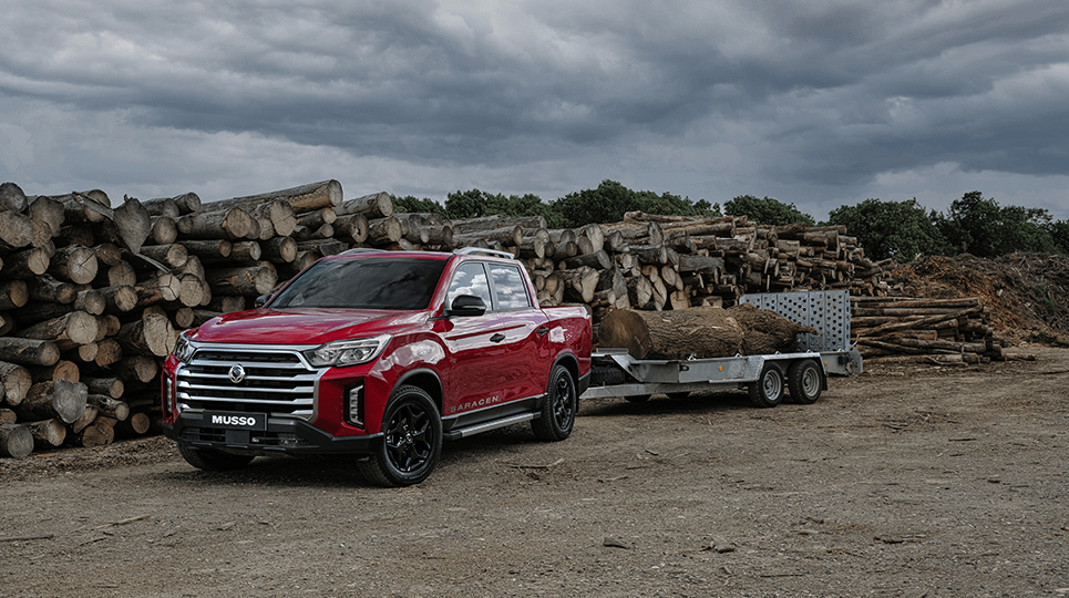 Red KGM Musso towing a trailer with logs in the background
