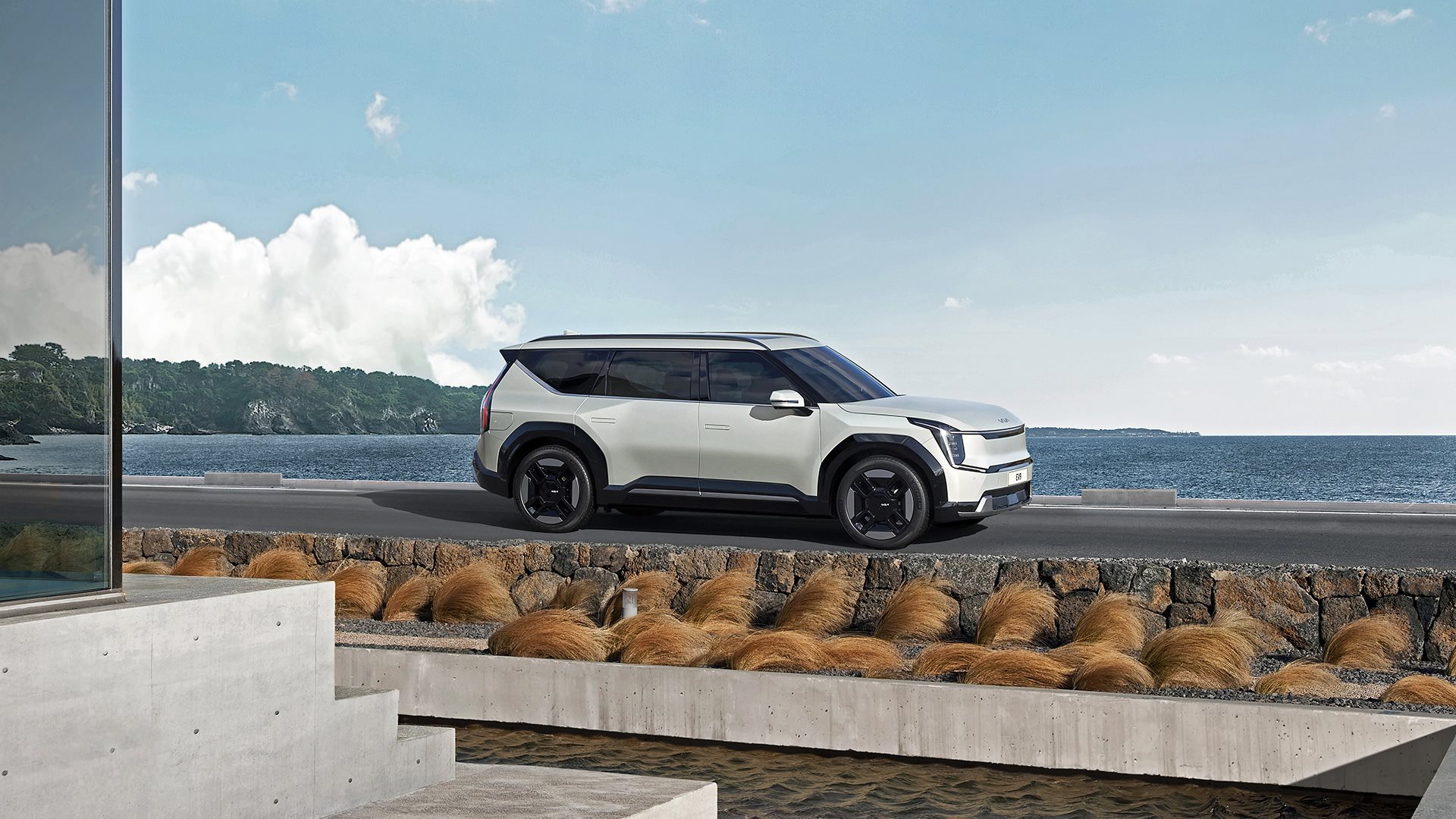 Side view of Kia EV9 parked on raised road with ocean in background