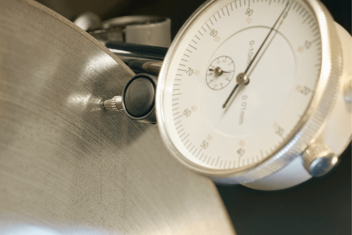 Dial gauge measuring brake disc thickness during vehicle inspection.