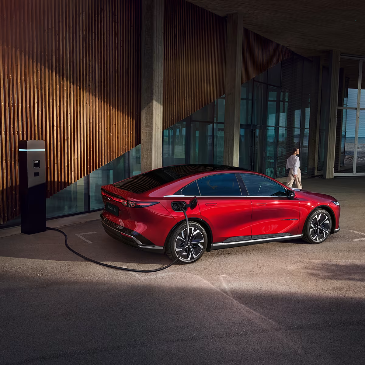 Mazda6e in red finish connected to an EV charger outside a business complex.