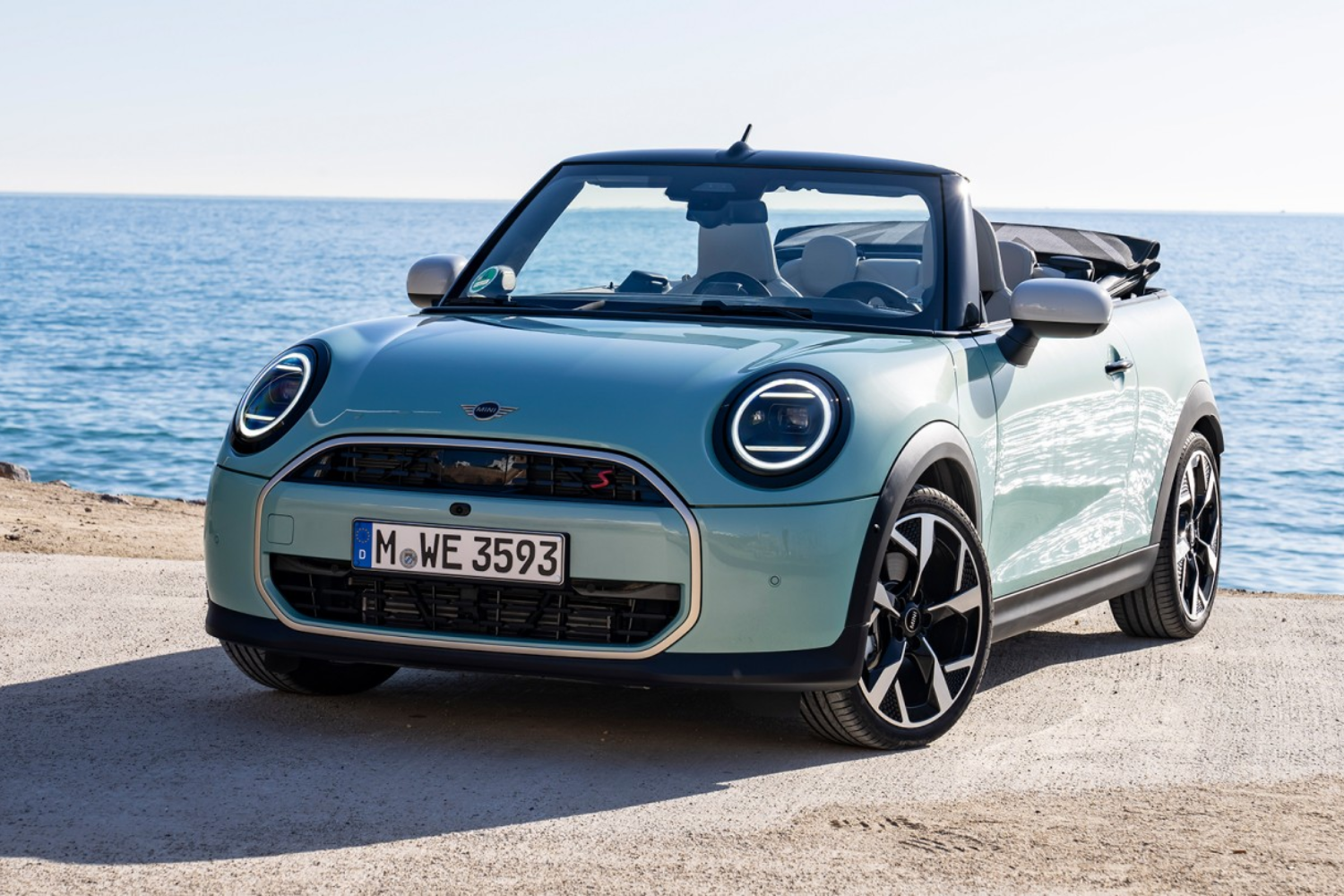 Mint green Mini Convertible parked by the sea.