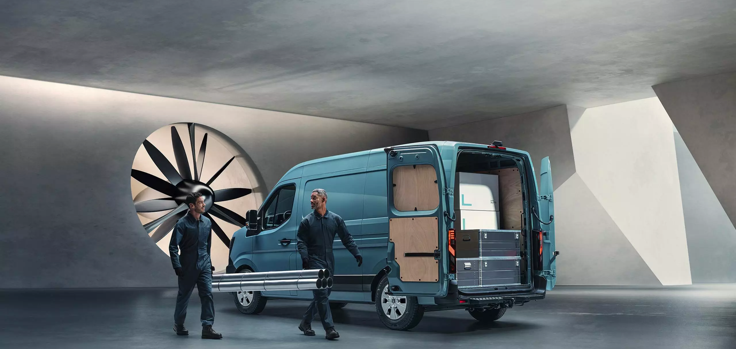 Rear three-quarter view of Renault Master van with doors open as workers carry pipes, highlighting practical loading space.