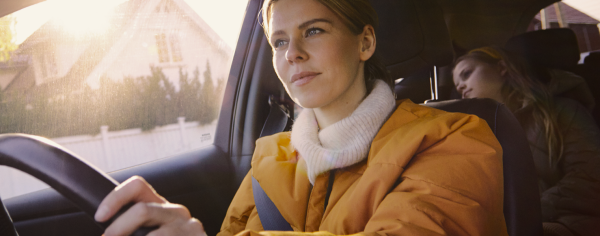 Close up of woman behind steering wheel with young girl in back seat