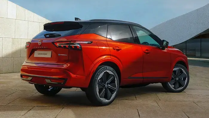 Red Nissan Qashqai SUV parked outside a modern building, shown from the rear three-quarter angle.