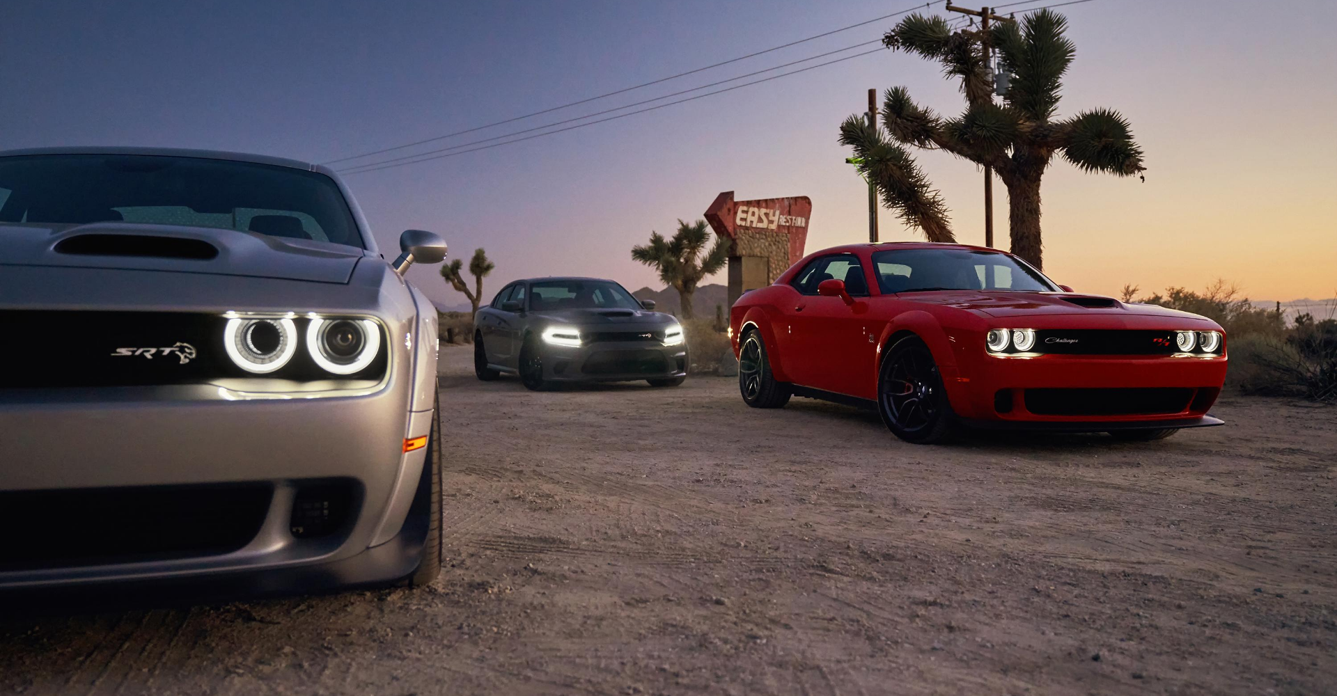 Dodge cars parked on dirt road at sunset