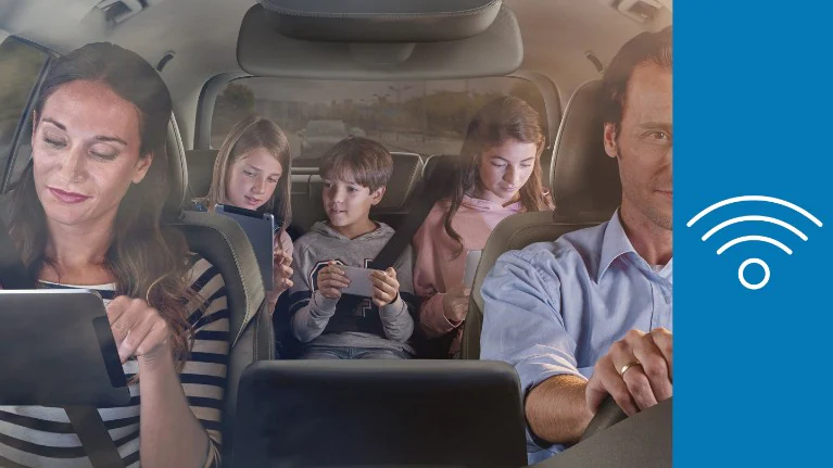 Passengers in a family car engaged with tablets and smartphones.