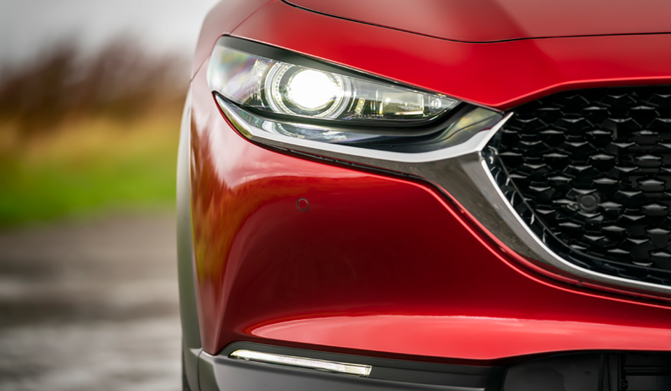 Front view of a red mazda cx-30 showing front grille with headlight on.