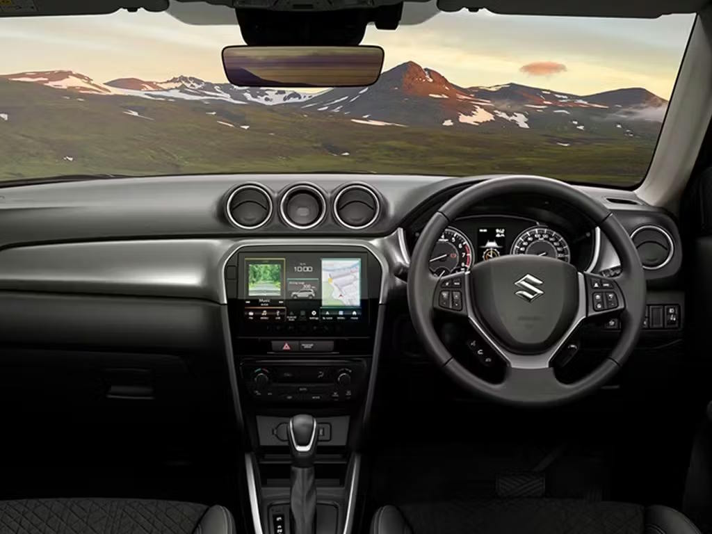 Interior view of the Suzuki Vitara dashboard, featuring a multifunction steering wheel, central touchscreen with navigation, circular air vents and analogue instrument cluster with dark trim.