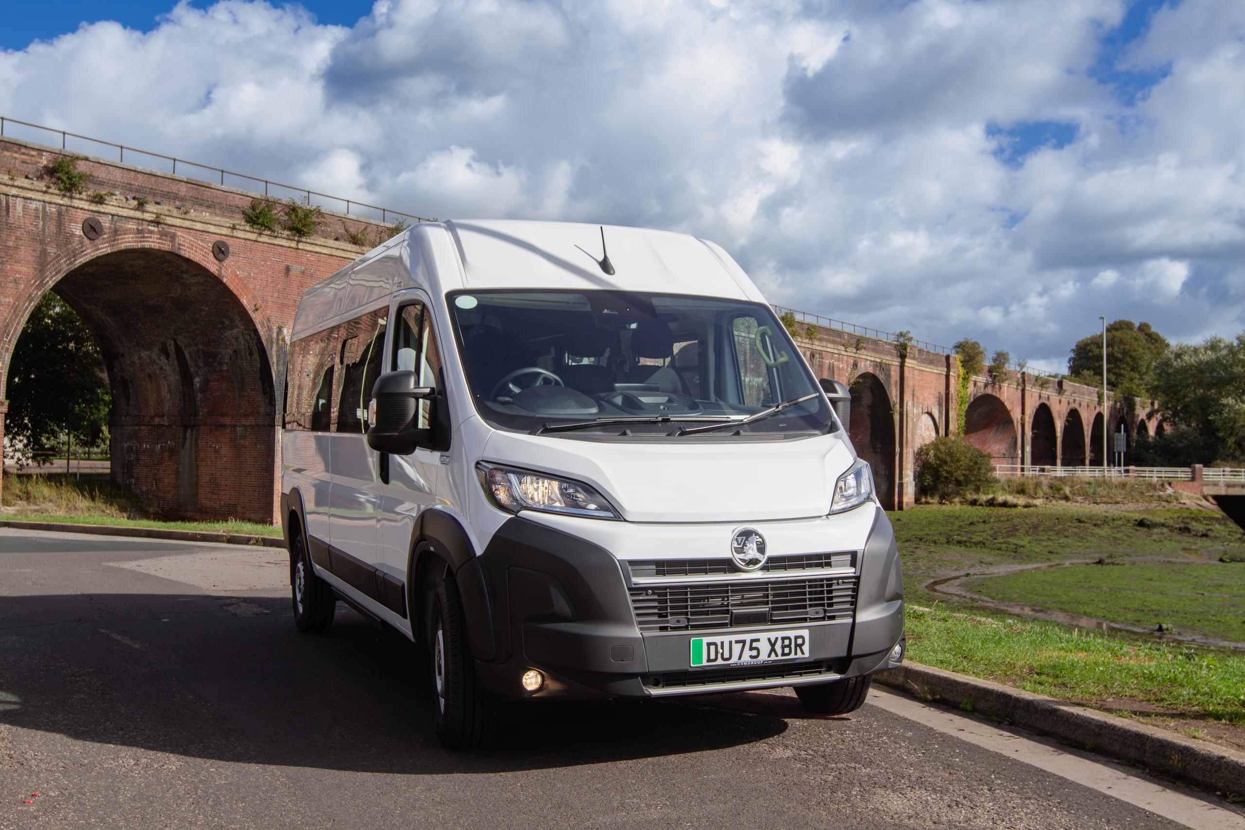 CVMinibus accessible minibus parked on a road beside a brick viaduct under blue sky.