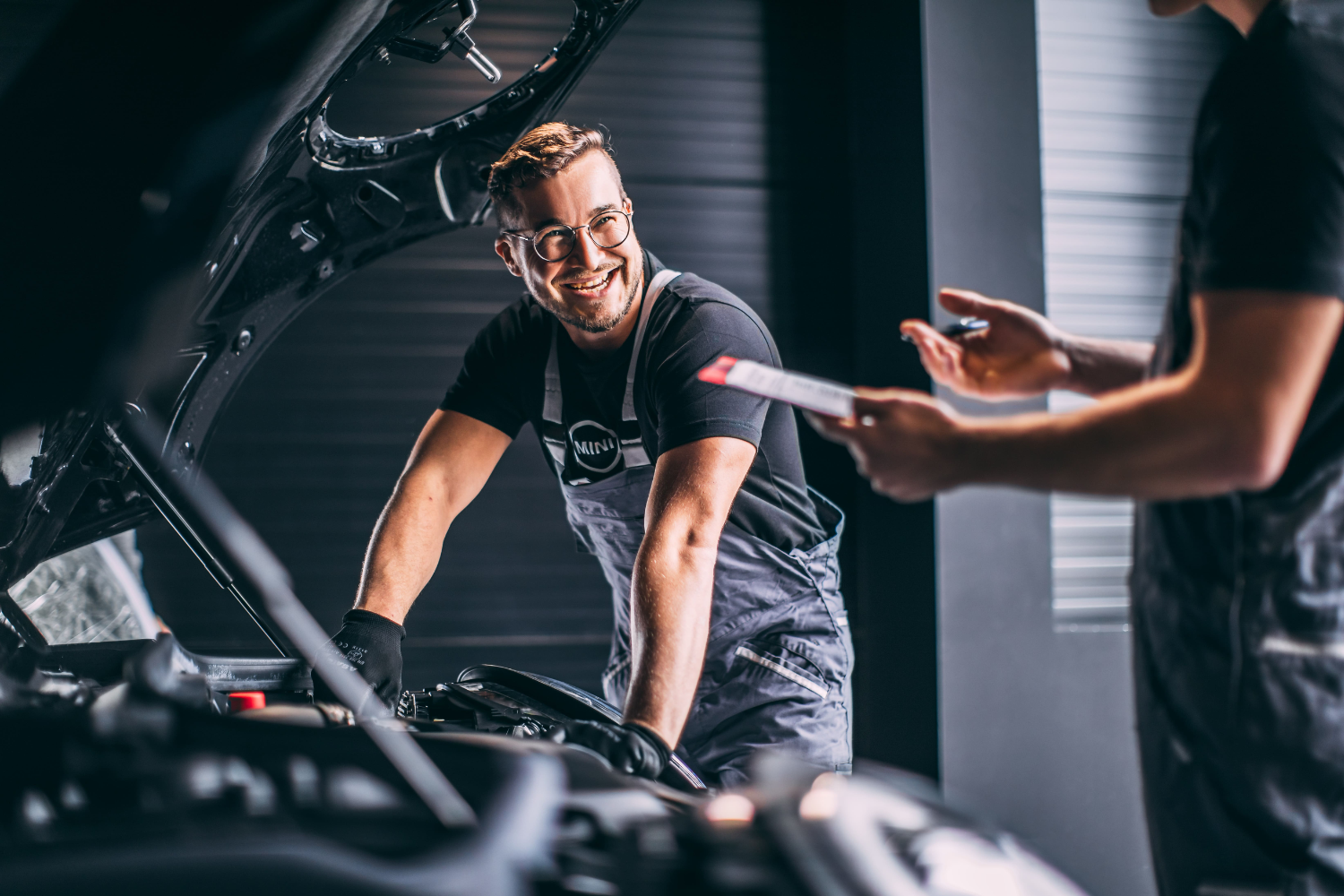Mechanic working under bonnet discussing vehicle service.