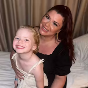Portrait of an adult and child sharing a cheerful moment in a bedroom setting.