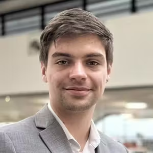 Professional portrait of a person wearing a light grey blazer in a modern office environment.