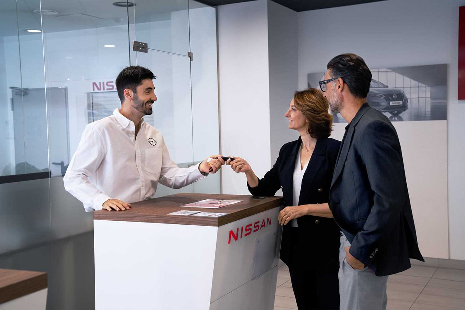 Nissan employee handing over keys to two customers stood at the counter